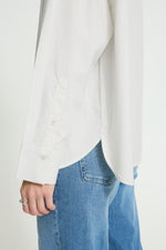 Blusa blanca con raya diplomática fina en marrón, cuello alto vuelto y botones decorativos. Un diseño elegante y versátil para tus looks de temporada.