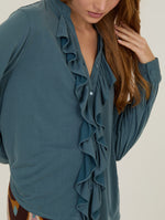 Camisa con volante frontal de manga larga confeccionada en un suave tejido fluido en color azul grisáceo.