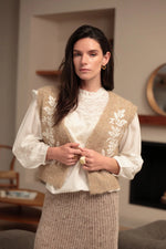 Chaleco de punto beige con bordados florales crudos y bajo acanalado sobre blusa blanca