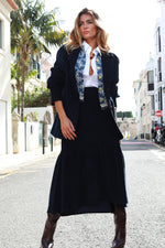 Falda midi de pana azul marino con bajo de volantes, combinada con chaqueta de punto color vino y botas altas